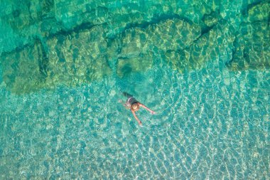 Top, aerial view. Young beautiful woman in white bikini swimming in sea water on the sand beach. Drone, copter photo. Summer vacation. View from above. 