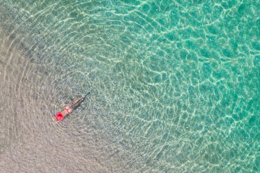 Üst Manzara. Kırmızı şapkalı ve bikinili genç bir kadın kumsalda deniz suyunda güneşleniyor. Drone, helikopter fotoğrafı. Yaz tatili. Yukarıdan görüntüle. 