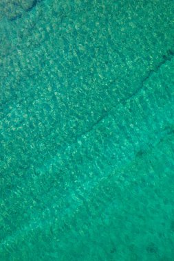 Background, texture of relaxing, calm turquoise, transparent sea water with stones, slabs, lump, coral. Summer vacation. Blue ocean lagoon. Drone, copter top view. 