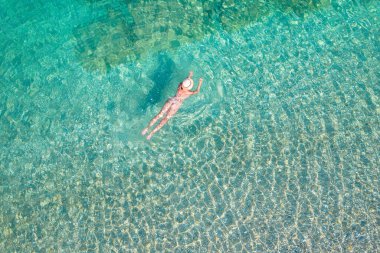 Top, aerial view. Young beautiful woman in a hat and white bikini swimming in sea water on the sand beach. Drone, copter photo. Summer vacation. View from above. 