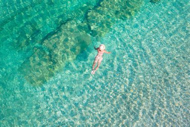 Top, aerial view. Young beautiful woman in a hat and white bikini swimming in sea water on the sand beach. Drone, copter photo. Summer vacation. View from above. 