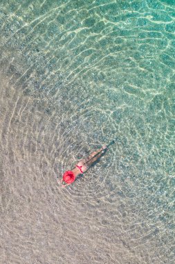 Top view. Young beautiful woman in a red hat and bikini lying and sunbathe in sea water on the sand beach. Drone, copter photo. Summer vacation. View from above. 