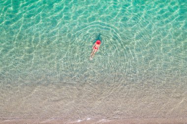 Üst Manzara. Kumsalda deniz suyunda yüzen kırmızı şapkalı ve bikinili güzel bir kadın. Drone, helikopter fotoğrafı. Yaz tatili. Yukarıdan görüntüle. 