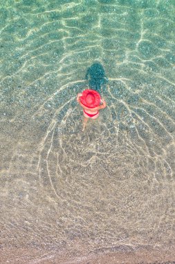 Top, aerial view. Young beautiful woman in a red hat and bikini walking, swimming, sunbathe in sea water on the sand beach. Drone, copter photo. Summer vacation. View from above. 