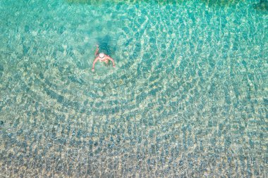 Top, aerial view. Young beautiful woman in a hat and white bikini swimming in sea water on the sand beach. Drone, copter photo. Summer vacation. View from above. 