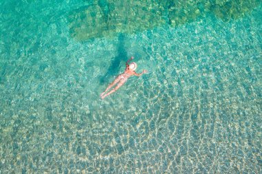 Top, aerial view. Young beautiful woman in a hat and white bikini swimming in sea water on the sand beach. Drone, copter photo. Summer vacation. View from above. 