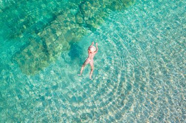 Top, aerial view. Young beautiful woman in a hat and white bikini swimming in sea water on the sand beach. Drone, copter photo. Summer vacation. View from above. 