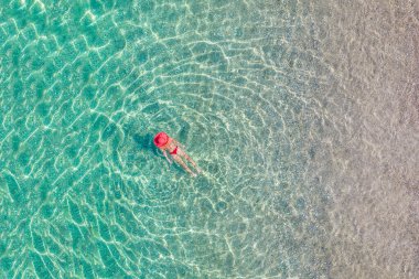 Top view. Young beautiful woman in a red hat and bikini swimming in sea water on the sand beach. Drone, copter photo. Summer vacation. View from above. 
