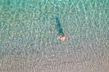Top view. Young beautiful naked woman in a hat taking off bikini in sea water. Drone, copter photo. Summer vacation. View from above.