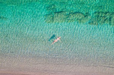 Top view. Young beautiful nudist woman with naked breast lying in sea water. Drone, copter photo. Summer vacation. View from above. 