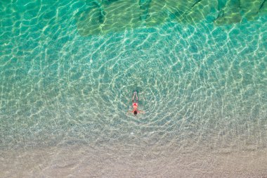 Üst, hava manzaralı. Kumsalda deniz suyunda yüzen kırmızı bikinili genç bir kadın. Drone, helikopter fotoğrafı. Yaz tatili. Yukarıdan görüntüle. 