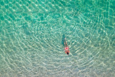 Top, aerial view. Young beautiful woman in a red bikini panties swimming in sea water on the sand beach. Drone, copter photo. Summer vacation. View from above. 