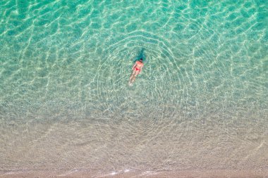 Üst, hava manzaralı. Kumsalda deniz suyunda yüzen kırmızı bikinili genç bir kadın. Drone, helikopter fotoğrafı. Yaz tatili. Yukarıdan görüntüle. 