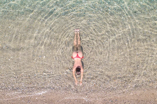 空中からの眺めだ 砂のビーチで海の水に横たわって日光浴をする赤いビキニパンティーの若い美しい女性 ドローン コッパー写真 夏休みだ 上からの眺め — ストック写真