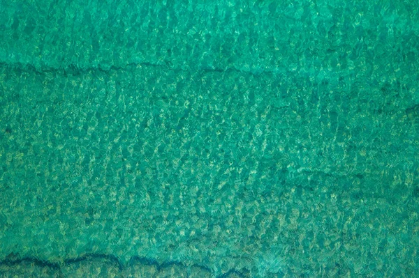Background, texture of relaxing, calm turquoise, transparent sea water with stones, slabs, lump, coral. Summer vacation. Blue ocean lagoon. Drone, copter top view. 