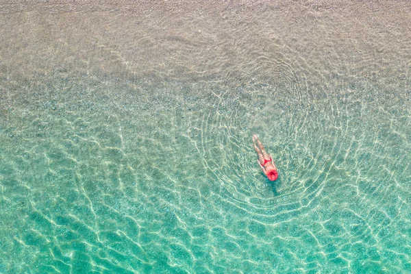 Üst Manzara. Kumsalda deniz suyunda yüzen kırmızı şapkalı ve bikinili güzel bir kadın. Drone, helikopter fotoğrafı. Yaz tatili. Yukarıdan görüntüle. 