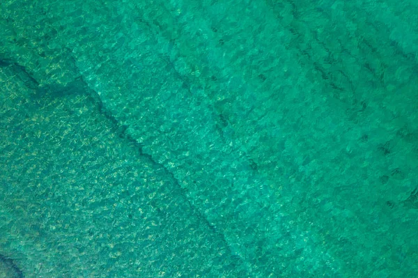 Background, texture of relaxing, calm turquoise, transparent sea water with stones, slabs, lump, coral. Summer vacation. Blue ocean lagoon. Drone, copter top view. 