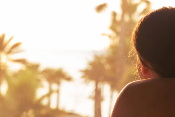 一个女人的画像躺在阳台上的日光浴床上 日落时看着棕榈树的海滩 女性放松 背景色 — 图库照片