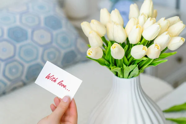 テーブルの上に白い花瓶に白いチューリップの花の花束から愛の言葉 テキスト と挨拶カードを引く女性 — ストック写真