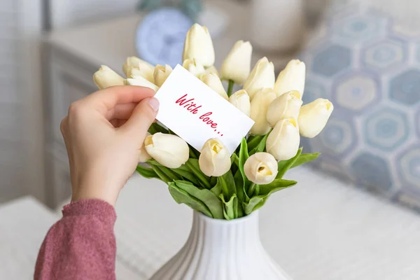 テーブルの上に白い花瓶に白いチューリップの花の花束から愛の言葉 テキスト と挨拶カードを引く女性 — ストック写真