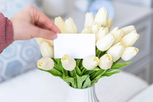白いチューリップの花の花束から空白の挨拶カードを引く女性 バレンタインデー コピースペース モックアップ — ストック写真