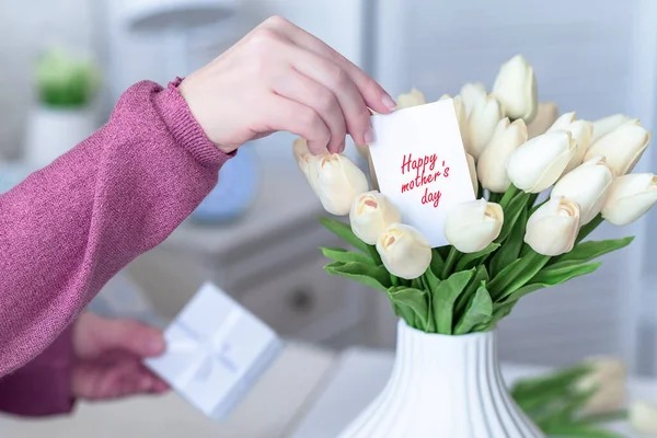 女が挨拶カードを引く幸せな母の日の言葉から花束の白いチューリップの花でテーブルの上に白い花瓶 — ストック写真