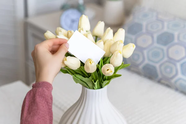 白いチューリップの花の花束から空白の挨拶カードを引く女性 コピースペース モックアップ — ストック写真