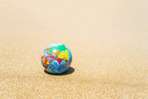 Игрушечный глобус на песке пляжа. Концепция путешествий по миру.