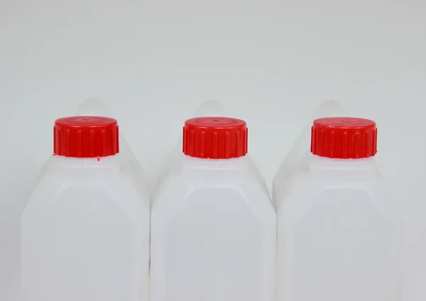 Three empty jerrycans of white plastic with red lids — Stock Photo, Image