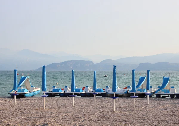 stock image Water cycles and parasols at empty beach in the morning