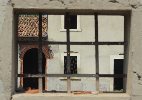 Ventana con barras de metal enmarcando una casa de campo abandonada —  Fotos de Stock