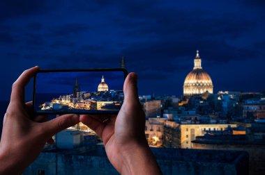 Valletta 'nın Valletta, Malta' daki eski kasaba ve limanında gece aydınlanan turistlerin fotoğraflarını çeken bir turist.