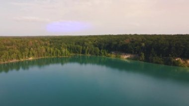 Aerial top-down flight over the amazing small lake of a perfectly round shape. Cloudy sky reflected in the clear turquoise water of a pond surrounded by trees and plants. 