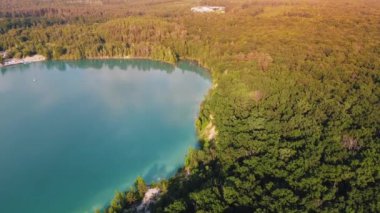 Aerial top-down flight over the amazing small lake of a perfectly round shape. Cloudy sky reflected in the clear turquoise water of a pond surrounded by trees and plants. 