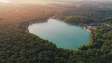 Aerial top-down flight over the amazing small lake of a perfectly round shape. Cloudy sky reflected in the clear turquoise water of a pond surrounded by trees and plants. 