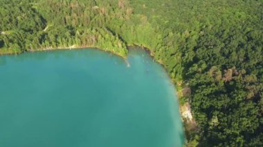 Aerial top-down flight over the amazing small lake of a perfectly round shape. Cloudy sky reflected in the clear turquoise water of a pond surrounded by trees and plants. 
