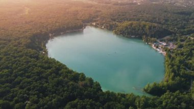 Aerial top-down flight over the amazing small lake of a perfectly round shape. Cloudy sky reflected in the clear turquoise water of a pond surrounded by trees and plants. 