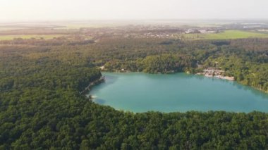 Aerial top-down flight over the amazing small lake of a perfectly round shape. Cloudy sky reflected in the clear turquoise water of a pond surrounded by trees and plants.