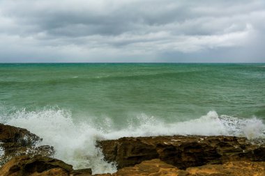 Kızgın turkuaz yeşil renk okyanus boyunca yuvarlanan dalgaların büyük kıvrımlı kıvrımları. Vahşi dalgalar fırtınalı bir günde Chabahar kıyılarını vuruyor bulutlu gökyüzü kıyıya yakın, Umman Denizi