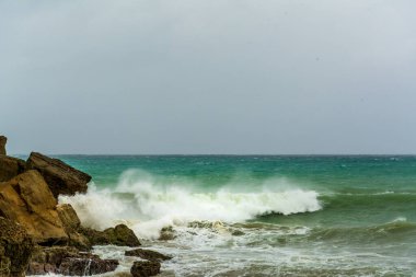 Kızgın turkuaz yeşil renk okyanus boyunca yuvarlanan dalgaların büyük kıvrımlı kıvrımları. Vahşi dalgalar fırtınalı bir günde Chabahar kıyılarını vuruyor bulutlu gökyüzü kıyıya yakın, Umman Denizi
