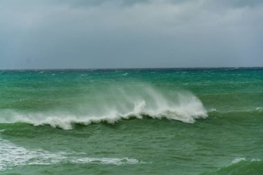 Kızgın turkuaz yeşil renk okyanus boyunca yuvarlanan dalgaların büyük kıvrımlı kıvrımları. Vahşi dalgalar fırtınalı bir günde Chabahar kıyılarını vuruyor bulutlu gökyüzü kıyıya yakın, Umman Denizi