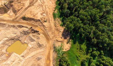 İnsafsız bir kum çukuru yeşil bir ormanın üzerinde çok az ağaç kalmış.