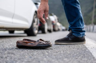 Bir adamın eli unutulmuş bir ayakkabıyı asfalttan kaldırıyor.