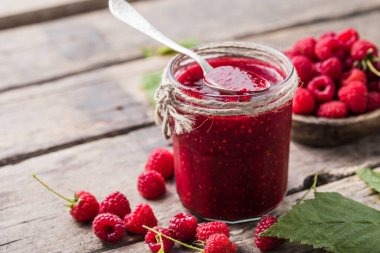 Ahşap arka planda ev yapımı ahududu reçeli, taze ahududu ve seçici bir odak noktası var..