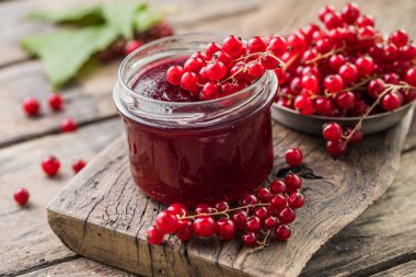 Kırmızı, sulu üzümlü frenk üzümü ve ahşap bir masada çilek reçeli kavanozu.