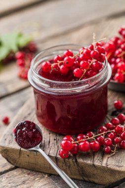Kırmızı, sulu üzümlü frenk üzümü ve ahşap bir masada çilek reçeli kavanozu.