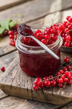 Kırmızı, sulu üzümlü frenk üzümü ve ahşap bir masada çilek reçeli kavanozu.