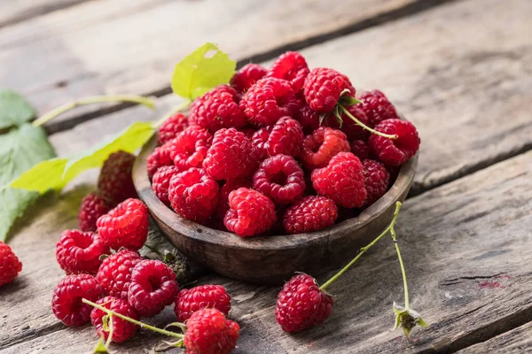 Tahta arka planda yeşil ahududu yapraklarıyla çevrili bir kasede sulu olgun ahududular. Boşluğu kopyala