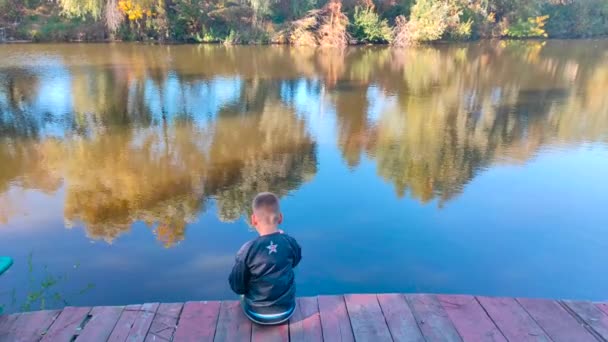 Вид сзади симпатичный мальчик глотает камень возле синей реки — стоковое видео
