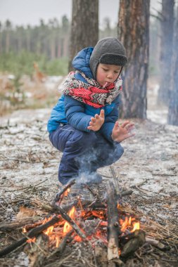 Güneşli kış ormanlarında, ateşin yanında yürüyüş yapan mutlu çocuk, Noel tatili.,